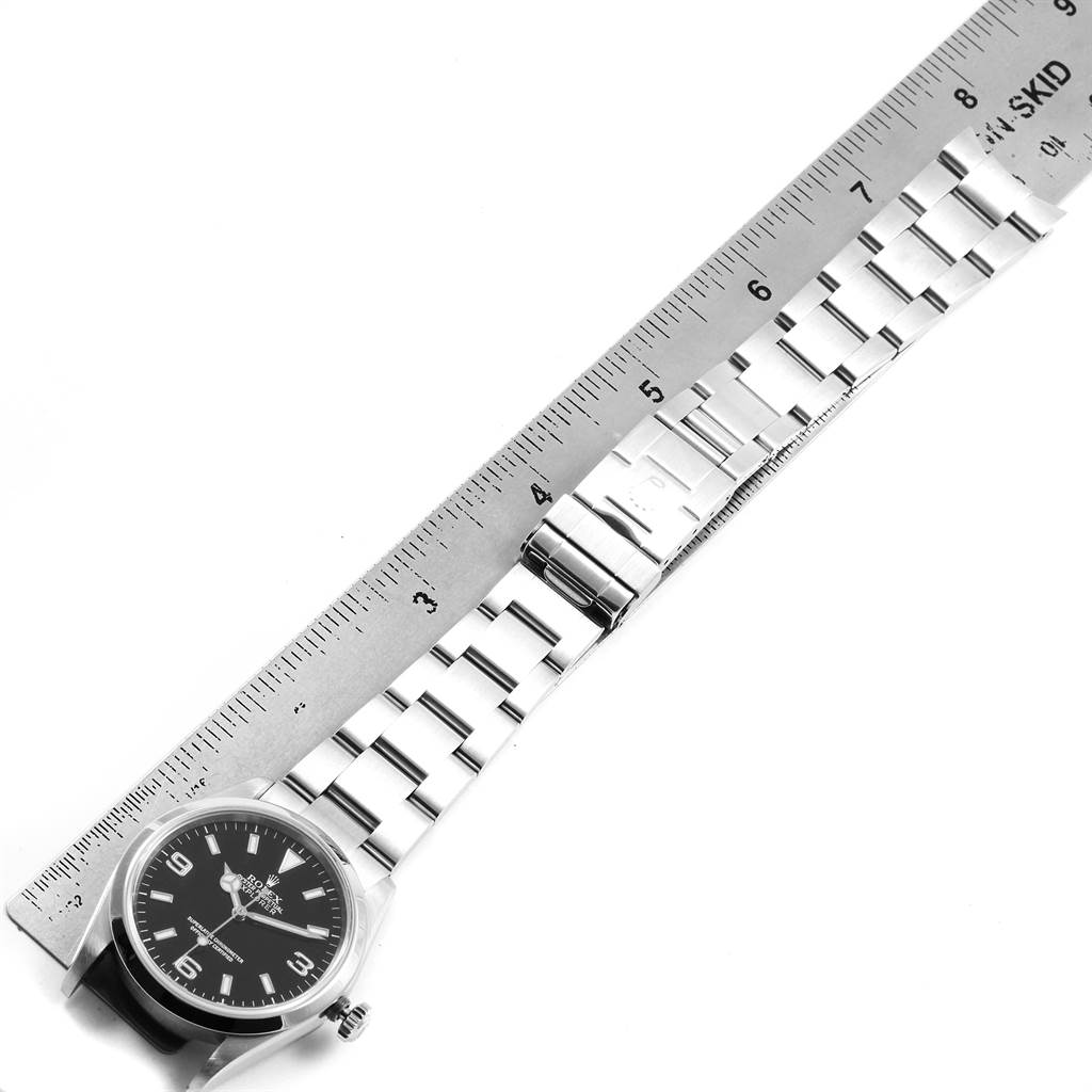 The Rolex Explorer 114270 Men's Stainless Steel Black Dial 114270 Men's Stainless Steel Black Dial watch is shown from an angled top view, displaying the face, bezel, bracelet, and part of the clasp alongside a ruler.