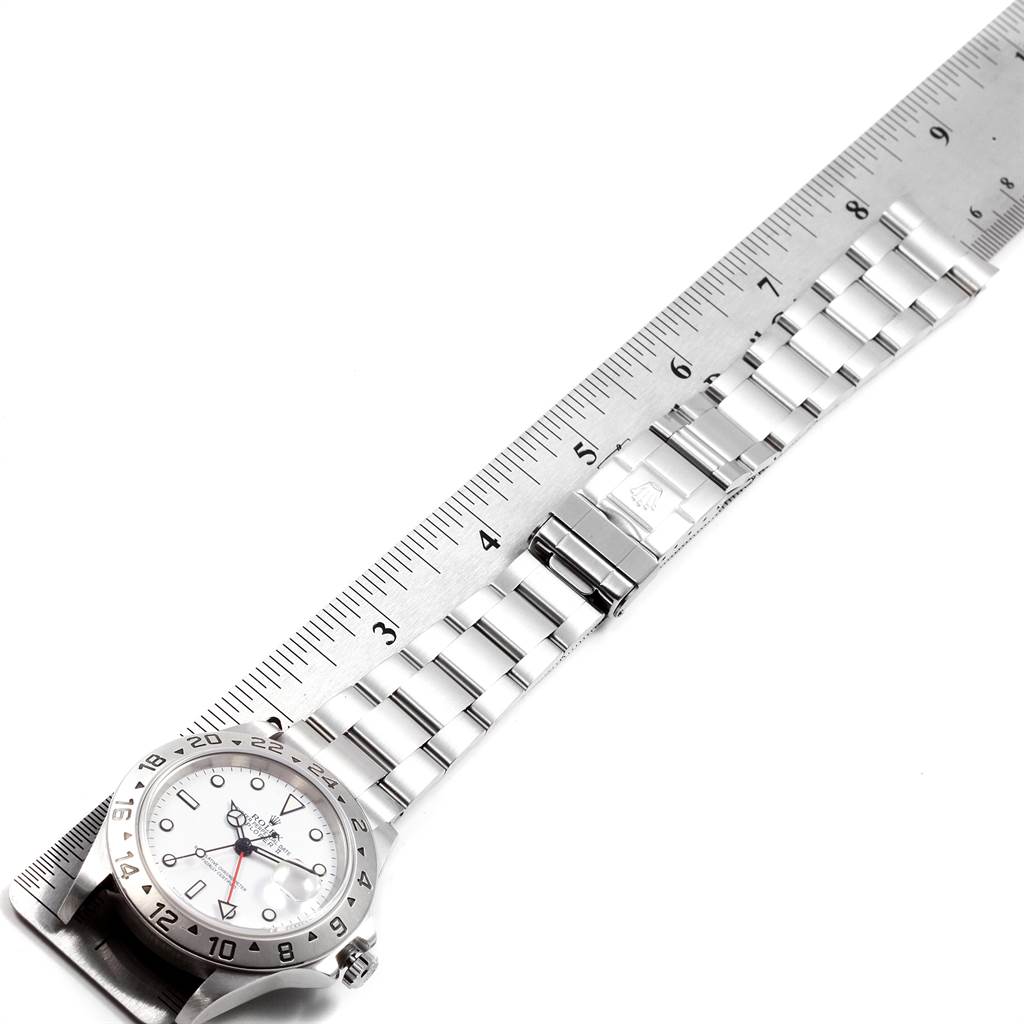 The image shows an overhead view of a Rolex Explorer 16570 Men's Stainless Steel White Dial 16570 Men's Stainless Steel White Dial watch with its band laid out next to a ruler.