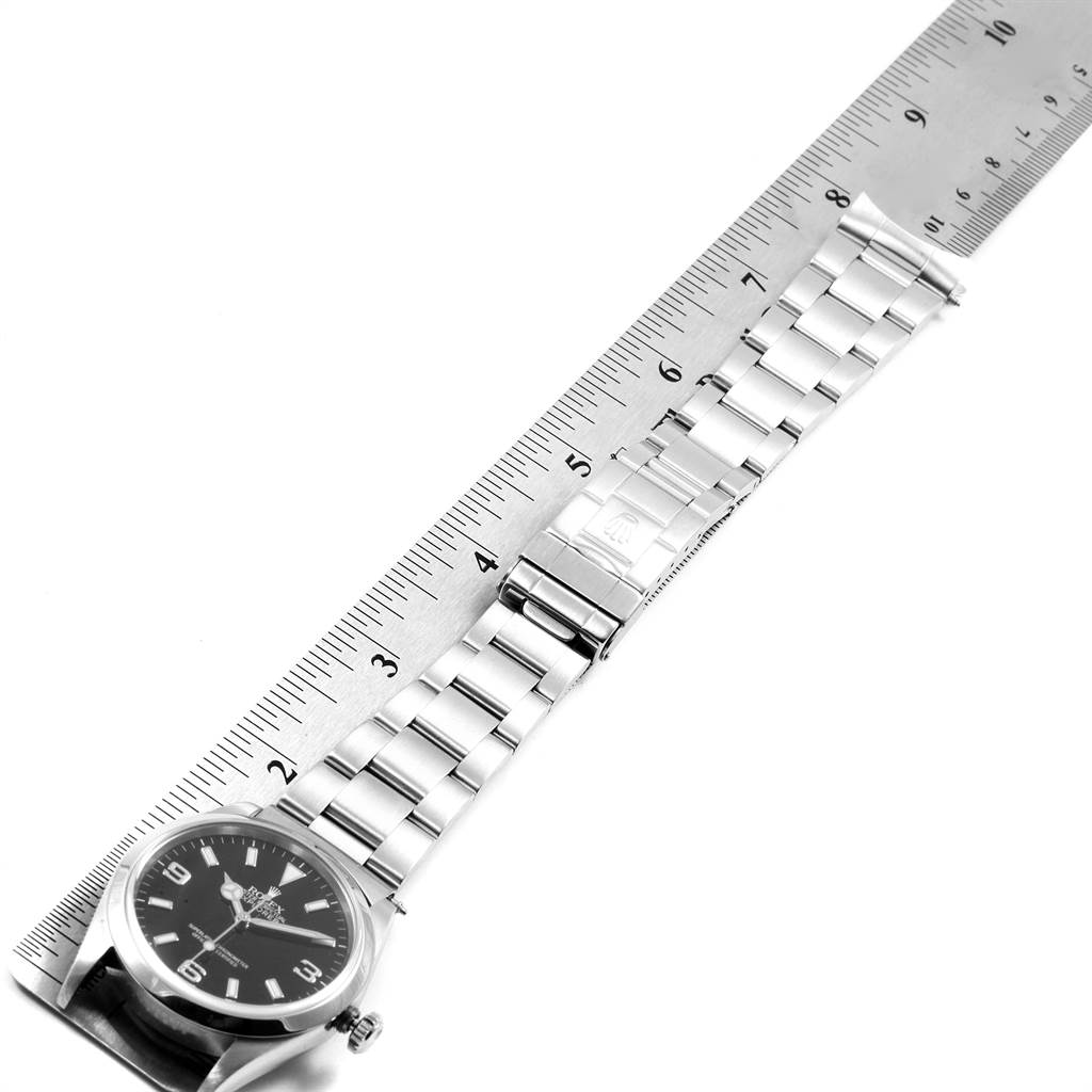The image shows a Rolex Explorer 14270 Men's Stainless Steel Black Dial 14270 Men's Stainless Steel Black Dial watch placed next to a ruler, highlighting its stainless steel bracelet and clasp.