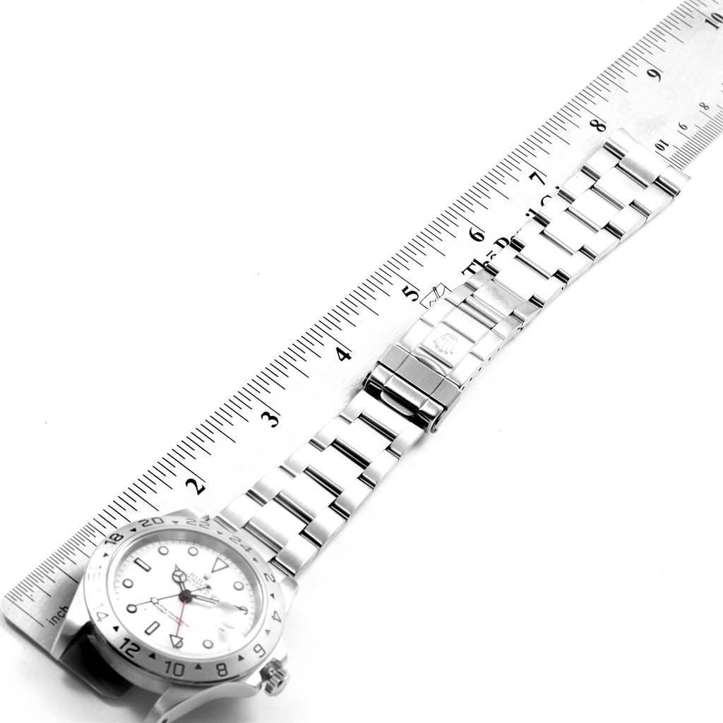 This image shows the Rolex Explorer 16570 Men's Stainless Steel White Dial 16570 Men's Stainless Steel White Dial watch laid flat with its band extended next to a ruler for measurement.