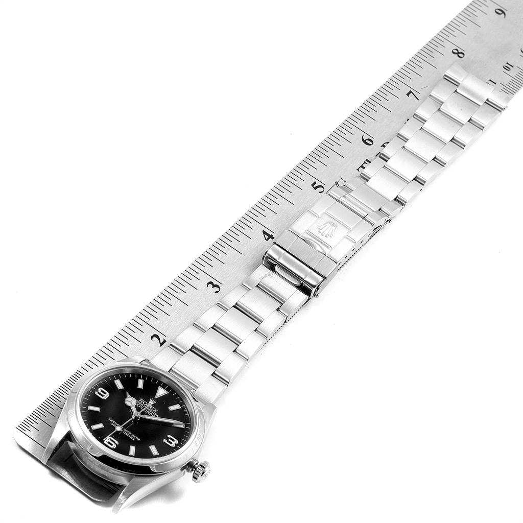 The image shows a top view of a Rolex Explorer 114270 Men's Stainless Steel Black Dial 114270 Men's Stainless Steel Black Dial watch laid next to a ruler, displaying the watch face and bracelet.