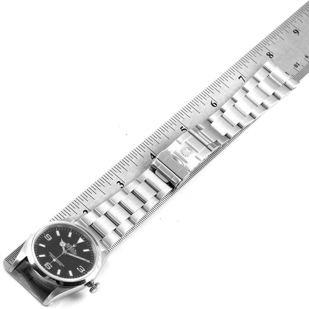 The image shows a Rolex Explorer Men's Stainless Steel Black Dial Men's Stainless Steel Black Dial watch positioned alongside a ruler, capturing its band and watch face from a top-down angle.