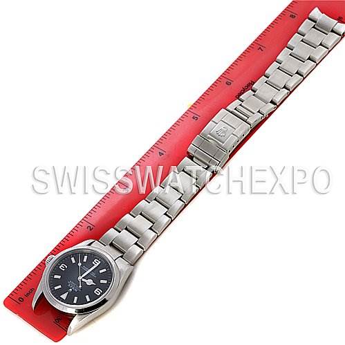 The image shows a top-down view of the Rolex Explorer 114270 Men
s Stainless Steel Black Dial 114270 Men
s Stainless Steel Black Dial watch, including its face and metal bracelet laid next to a red ruler.