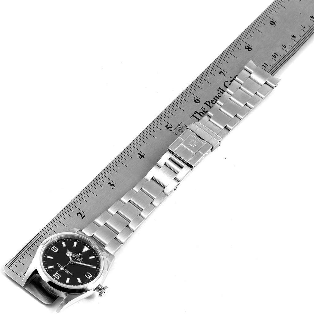 The image shows a side view of the Rolex Explorer 114270 Men's Stainless Steel Black Dial 114270 Men's Stainless Steel Black Dial watch and its metal bracelet laid next to a ruler.