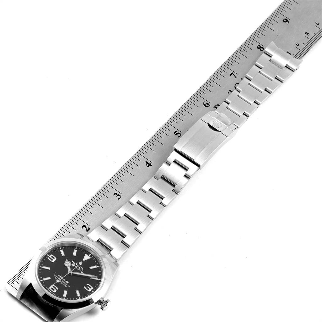 The image shows a top-down view of the Rolex Explorer 214270 Men
s Stainless Steel Black Dial 214270 Men
s Stainless Steel Black Dial watch with its bracelet extended and lying next to a ruler.