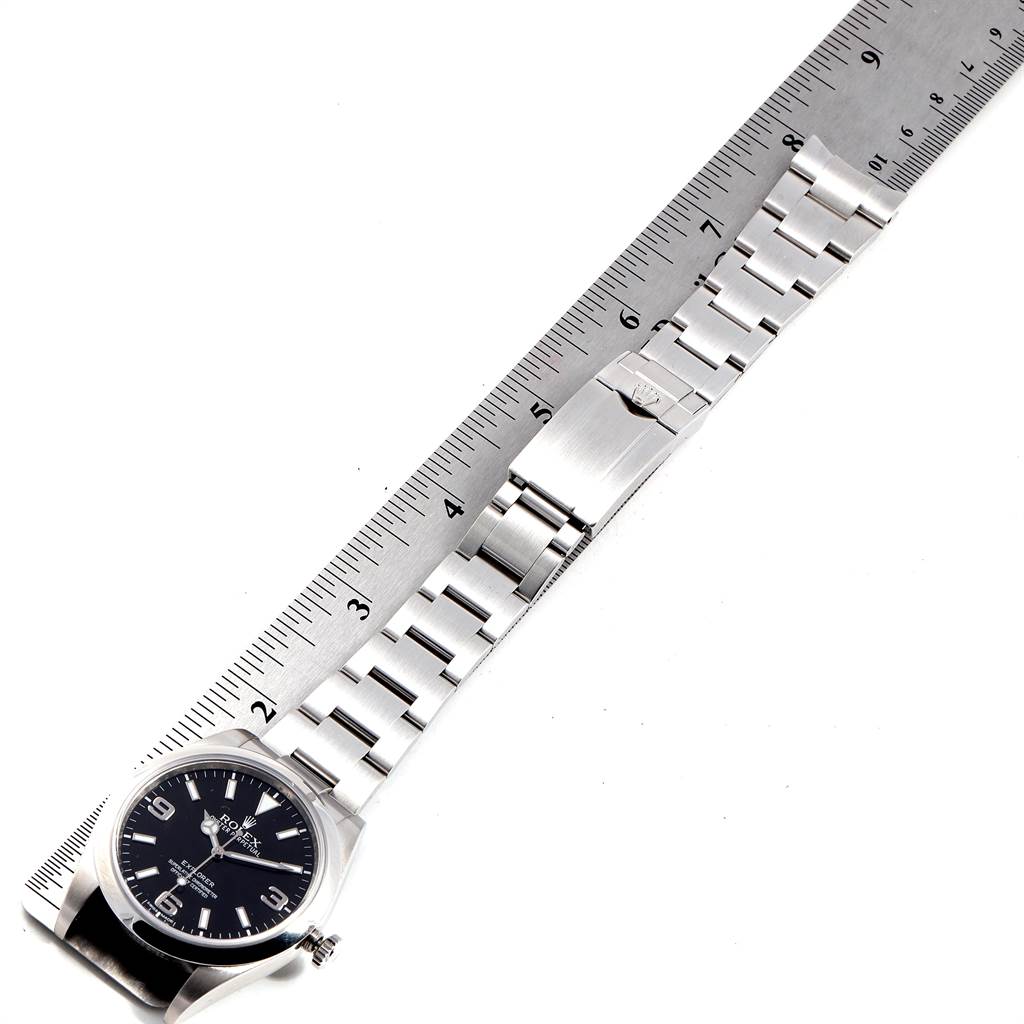 The Rolex Explorer 214270 Men's Stainless Steel Black Dial 214270 Men's Stainless Steel Black Dial watch is shown from a top-down angle, featuring the face, bracelet, and clasp, with a ruler for scale.