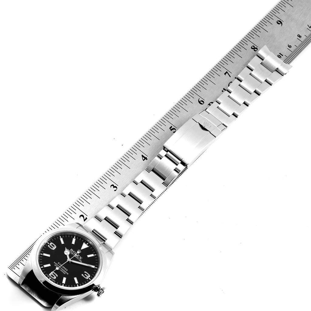 The image shows a Rolex Explorer 214270 Men's Stainless Steel Black Dial 214270 Men's Stainless Steel Black Dial watch laid flat on its band beside a ruler, displaying the face, bracelet, and clasp.