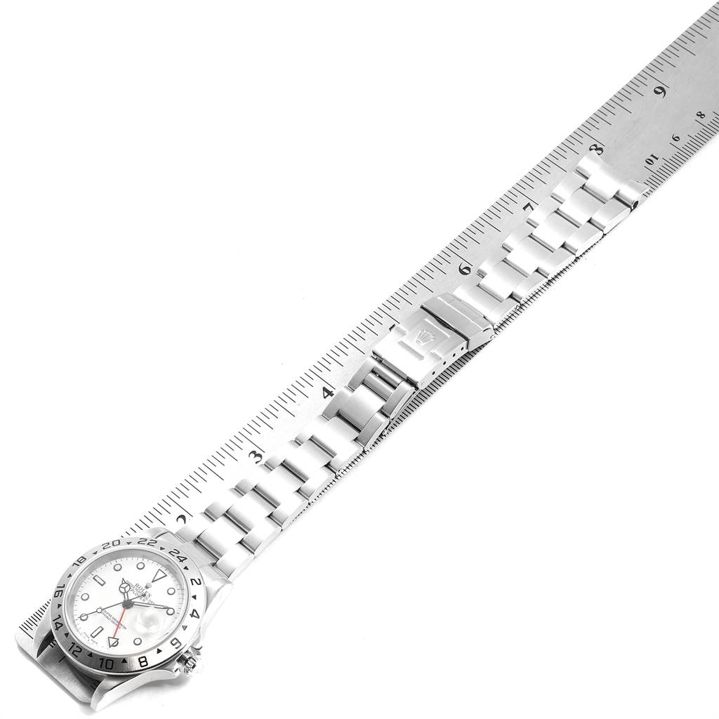 This image shows a Rolex Explorer 16570 Men's Stainless Steel White Dial 16570 Men's Stainless Steel White Dial watch laid flat alongside a ruler, highlighting its bracelet, clasp, and partially the face.