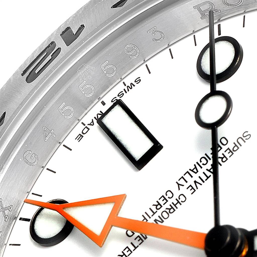 This close-up image of the Rolex Explorer 216570 Men's Stainless Steel White Dial 216570 Men's Stainless Steel White Dial watch shows part of the dial, hands, markers, and bezel with engraved numbers.