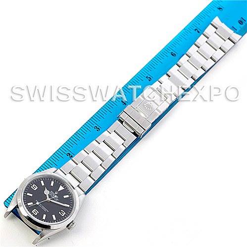 The Rolex Explorer 114270 Men's Stainless Steel Black Dial 114270 Men's Stainless Steel Black Dial watch is shown laid flat next to a blue ruler, displaying its face, bracelet, and clasp.