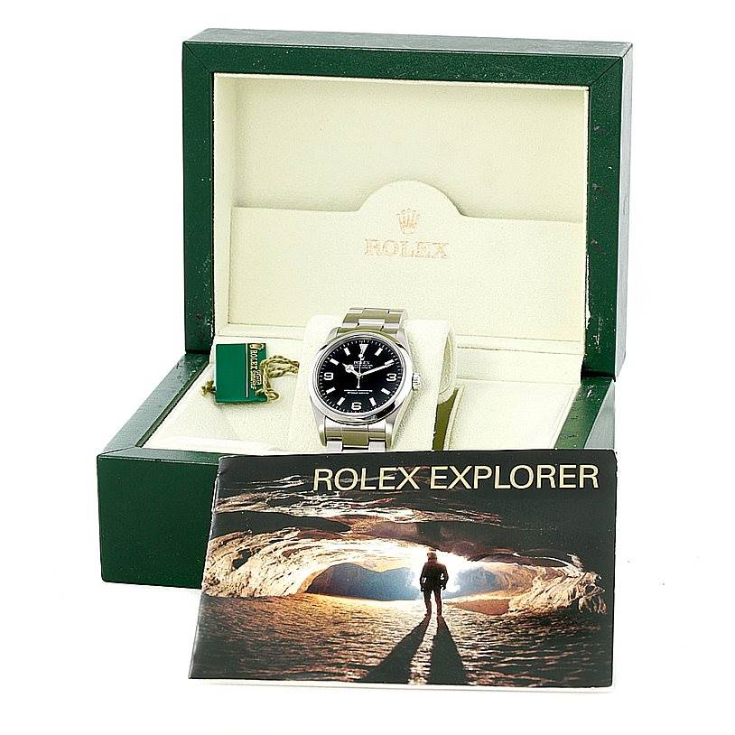 The Rolex Explorer 114270 Men's Stainless Steel Black Dial 114270 Men's Stainless Steel Black Dial watch is shown front-facing in its green case, accompanied by a booklet and a tag.