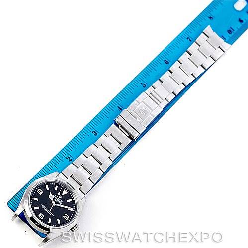 The Rolex Explorer 114270 Men's Stainless Steel Black Dial 114270 Men's Stainless Steel Black Dial watch is shown from a top-down angle, displaying its face, bracelet, and clasp next to a blue ruler.