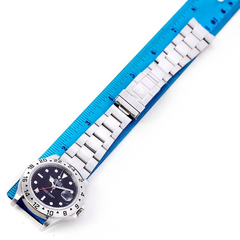 The Rolex Explorer 16570 Men
s Stainless Steel Black Dial 16570 Men
s Stainless Steel Black Dial watch is shown in a top-down angle, featuring the watch face, bezel, and bracelet laid next to a ruler.