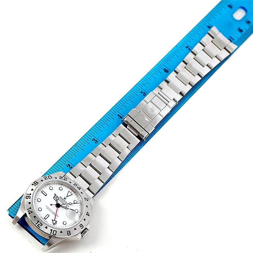 The Rolex Explorer 16570 Men's Stainless Steel White Dial 16570 Men's Stainless Steel White Dial watch is shown from a top-down angle, alongside a blue ruler, displaying its face, bezel, and bracelet.