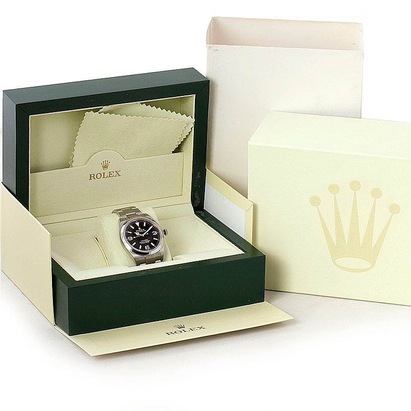 This image displays a Rolex Explorer 214270 Men's Stainless Steel Black Dial 214270 Men's Stainless Steel Black Dial watch in its box, along with the outer packaging and a cleaning cloth.