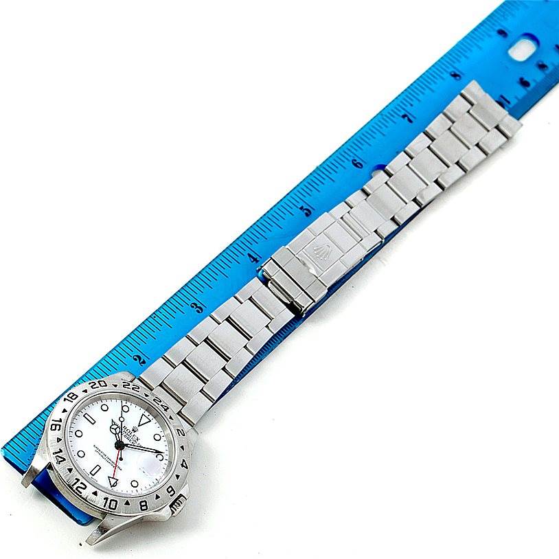 The image shows a Rolex Explorer 16570 Men's Stainless Steel White Dial 16570 Men's Stainless Steel White Dial watch laid flat with its bracelet extended alongside a blue ruler.