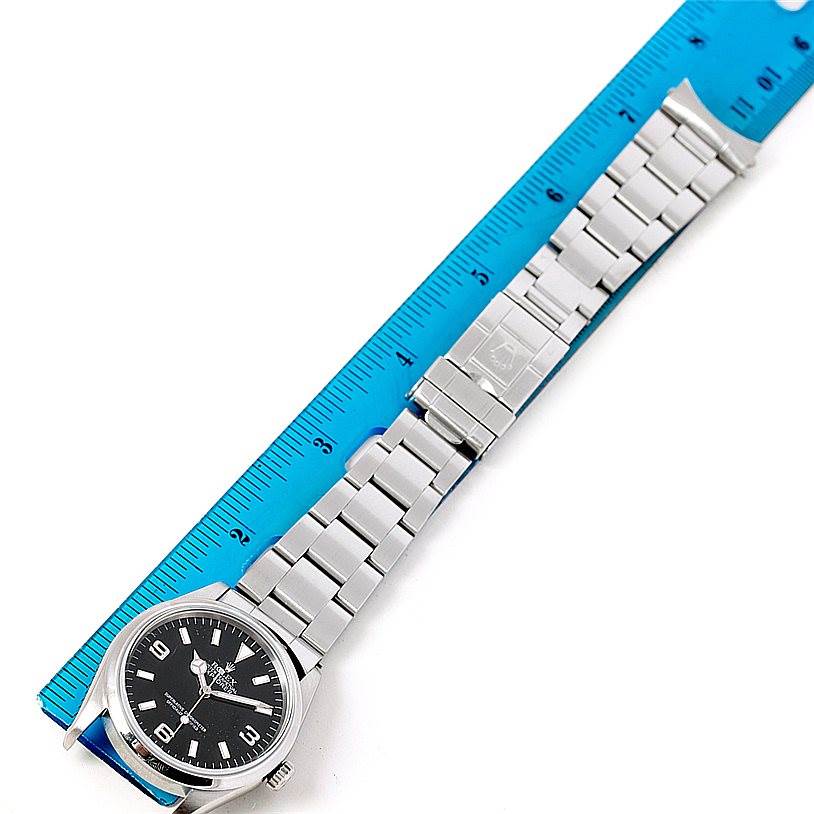 This image shows a top view of a Rolex Explorer 14270 Men's Stainless Steel Black Dial 14270 Men's Stainless Steel Black Dial watch with its stainless steel bracelet next to a blue ruler for scale.