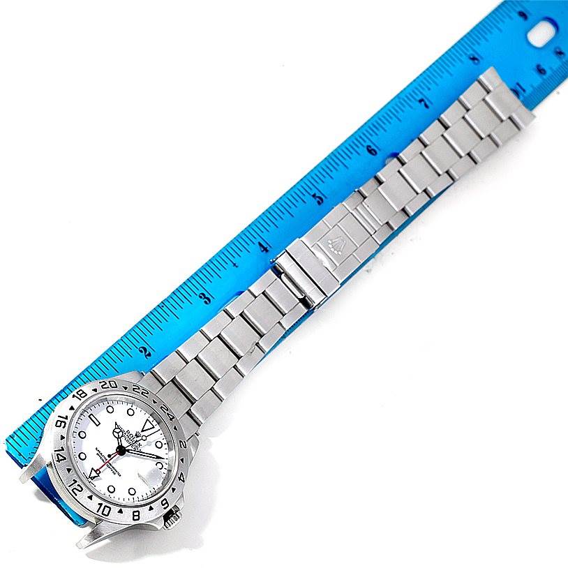 The image shows a top-down view of a Rolex Explorer 16570 Men's Stainless Steel White Dial 16570 Men's Stainless Steel White Dial watch with its bracelet fully extended next to a blue ruler.