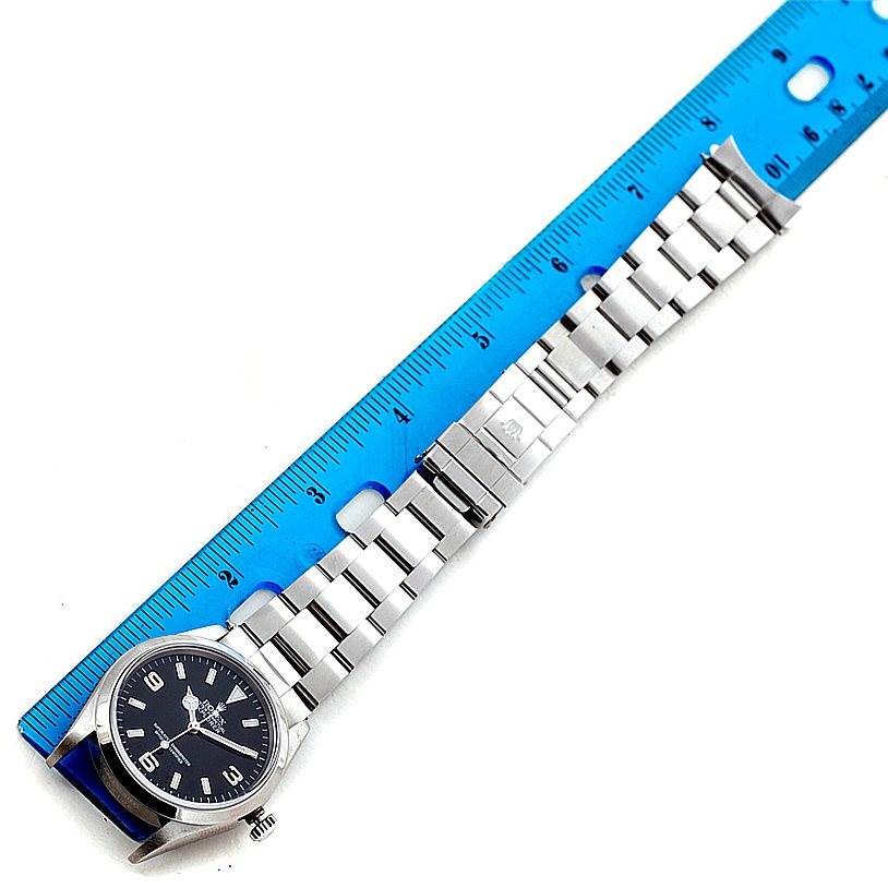 The image shows a top view of a Rolex Explorer 14270 Men's Stainless Steel Black Dial 14270 Men's Stainless Steel Black Dial watch with a blue measuring ruler beside it for scale.