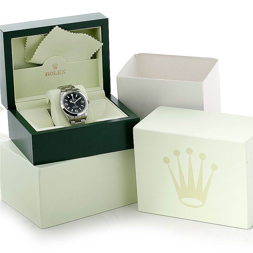 The image shows a Rolex Explorer 214270 Men's Stainless Steel Black Dial 214270 Men's Stainless Steel Black Dial watch in an open box, along with its outer box and cleaning cloth.