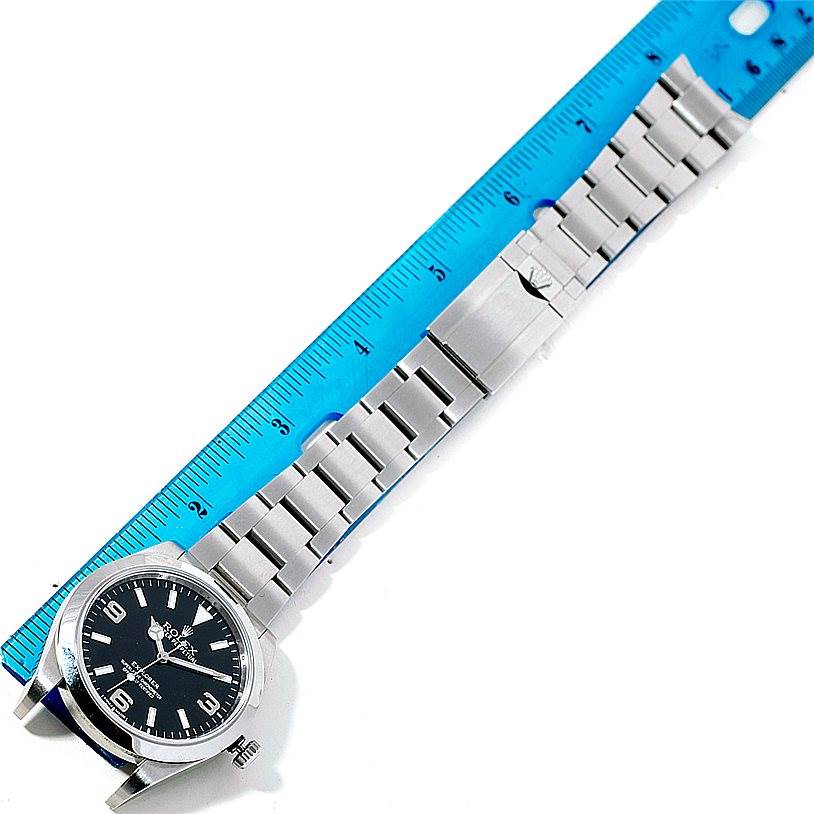 The image shows a Rolex Explorer 214270 Men's Stainless Steel Black Dial 214270 Men's Stainless Steel Black Dial watch laid flat beside a ruler, displaying the bracelet and clasp with the face at an angle.