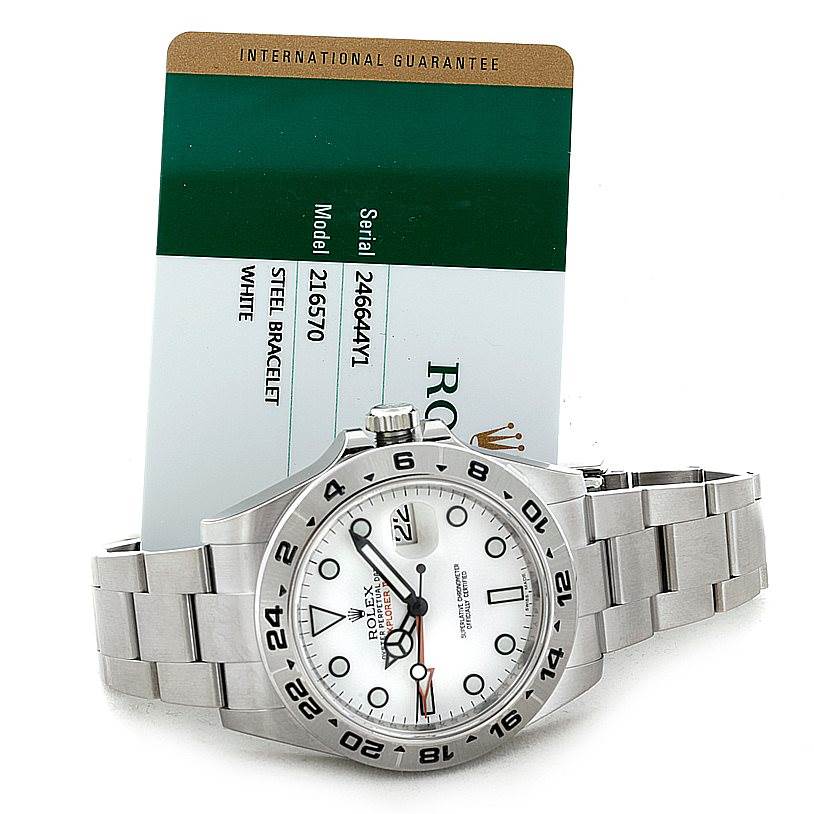 This image shows a Rolex Explorer 216570 Men's Stainless Steel White Dial 216570 Men's Stainless Steel White Dial watch laid flat with its bracelet extended and an international guarantee card in the background.
