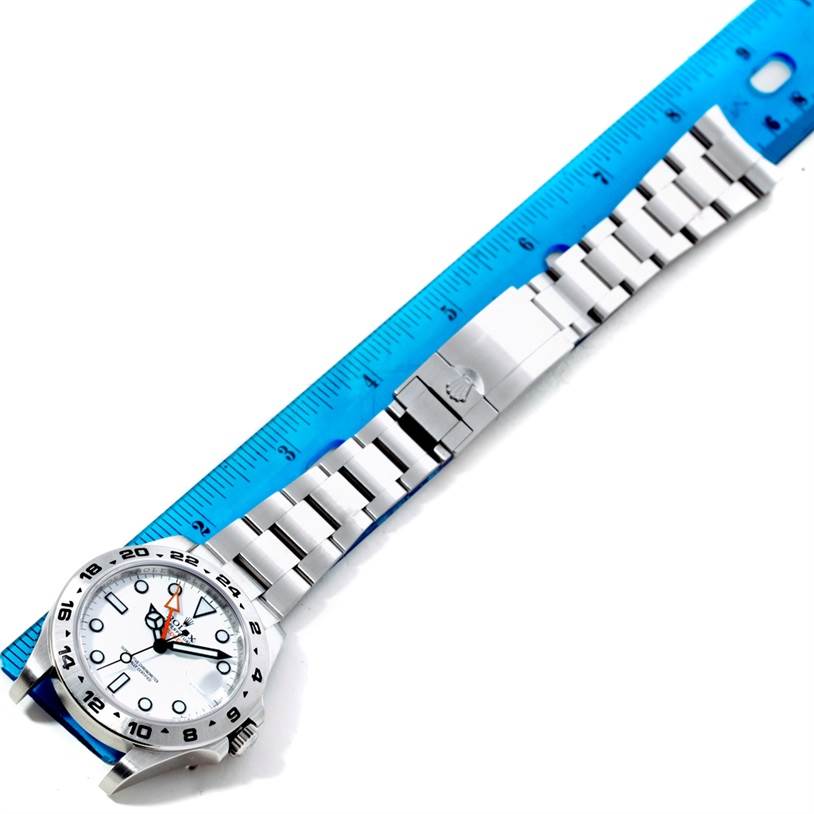 The image shows a Rolex Explorer 216570 Men's Stainless Steel White Dial 216570 Men's Stainless Steel White Dial watch with its full bracelet and clasp laid out beside a blue ruler.