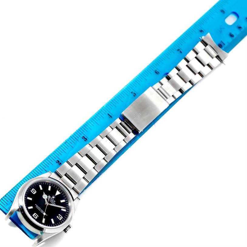 The image shows a Rolex Explorer 14270 Men's Stainless Steel Black Dial 14270 Men's Stainless Steel Black Dial watch laid horizontally with its stainless steel bracelet fully extended next to a blue ruler.