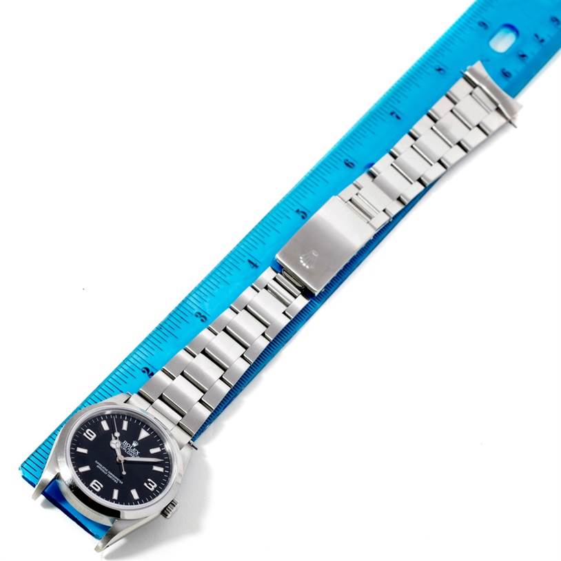 The image shows a top-down view of the Rolex Explorer 14270 Men's Stainless Steel Black Dial 14270 Men's Stainless Steel Black Dial watch, displaying the face, strap, and clasp, next to a blue ruler for scale.