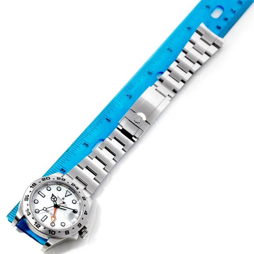 The image shows a Rolex Explorer 216570 Men
s Stainless Steel White Dial 216570 Men
s Stainless Steel White Dial watch laid flat, displaying the face, bezel, and full metal bracelet beside a blue ruler.