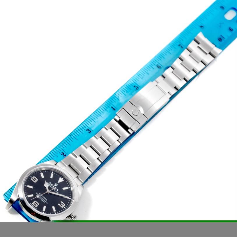 The image shows a top-down view of a Rolex Explorer 214270 Men's Stainless Steel Black Dial 214270 Men's Stainless Steel Black Dial watch, including its face, bracelet, and clasp, with a ruler for scale.