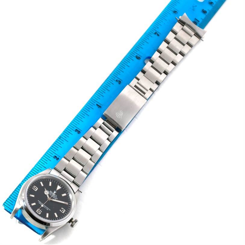 The Rolex Explorer 14270 Men's Stainless Steel Black Dial 14270 Men's Stainless Steel Black Dial watch is shown laid flat with a metal band, alongside a ruler for measurement.