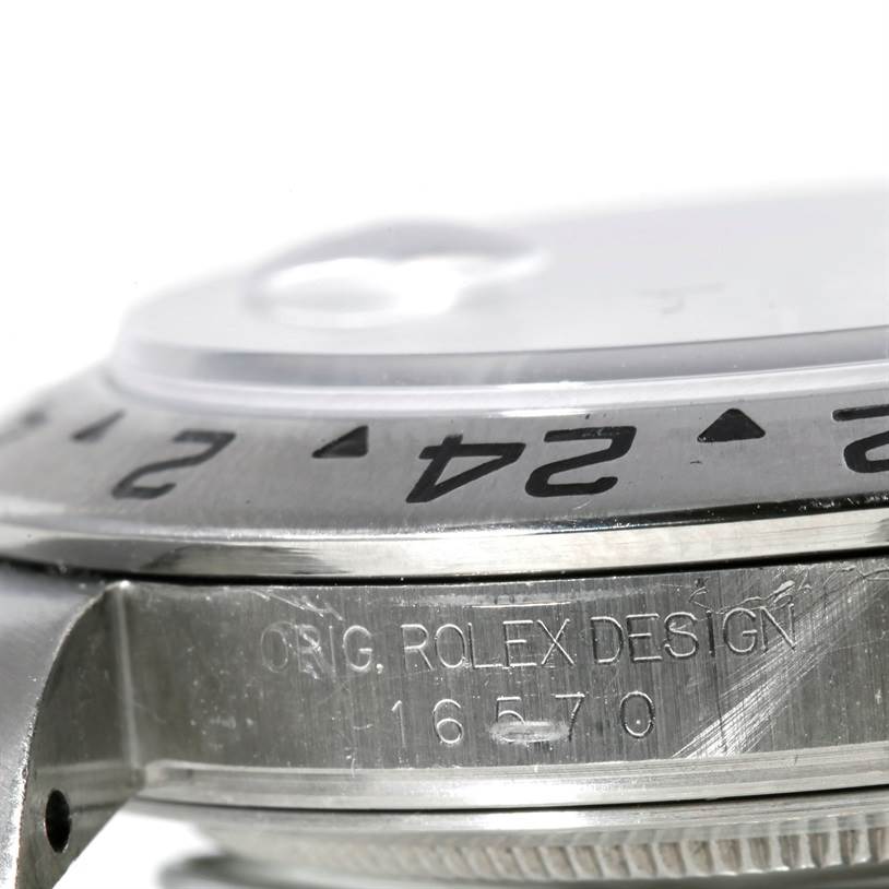 This close-up image of a Rolex Explorer 16570 Men's Stainless Steel White Dial 16570 Men's Stainless Steel White Dial watch shows part of the bezel, crown, and engraved case details.