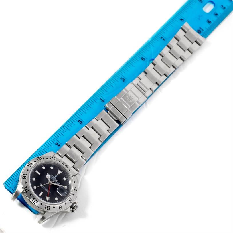 The Rolex Explorer 16570 Men's Stainless Steel Black Dial 16570 Men's Stainless Steel Black Dial watch is shown laid flat next to a blue ruler, displaying its bracelet and face prominently.