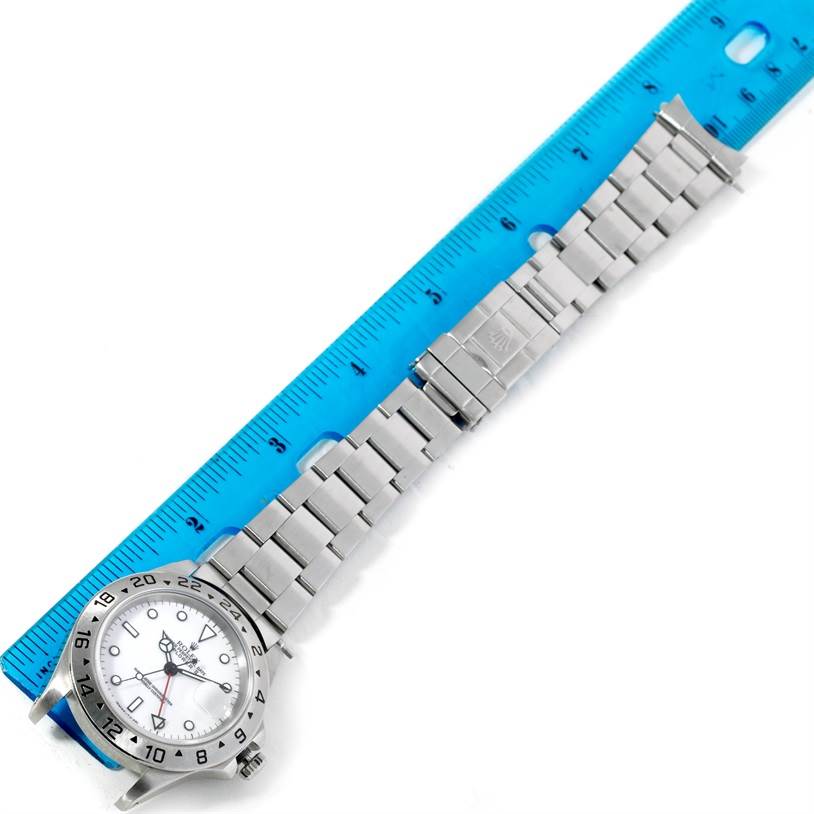 The image shows a top-down view of a Rolex Explorer 16570 Men's Stainless Steel White Dial 16570 Men's Stainless Steel White Dial watch with its metal band laid out alongside a blue ruler for measurement.