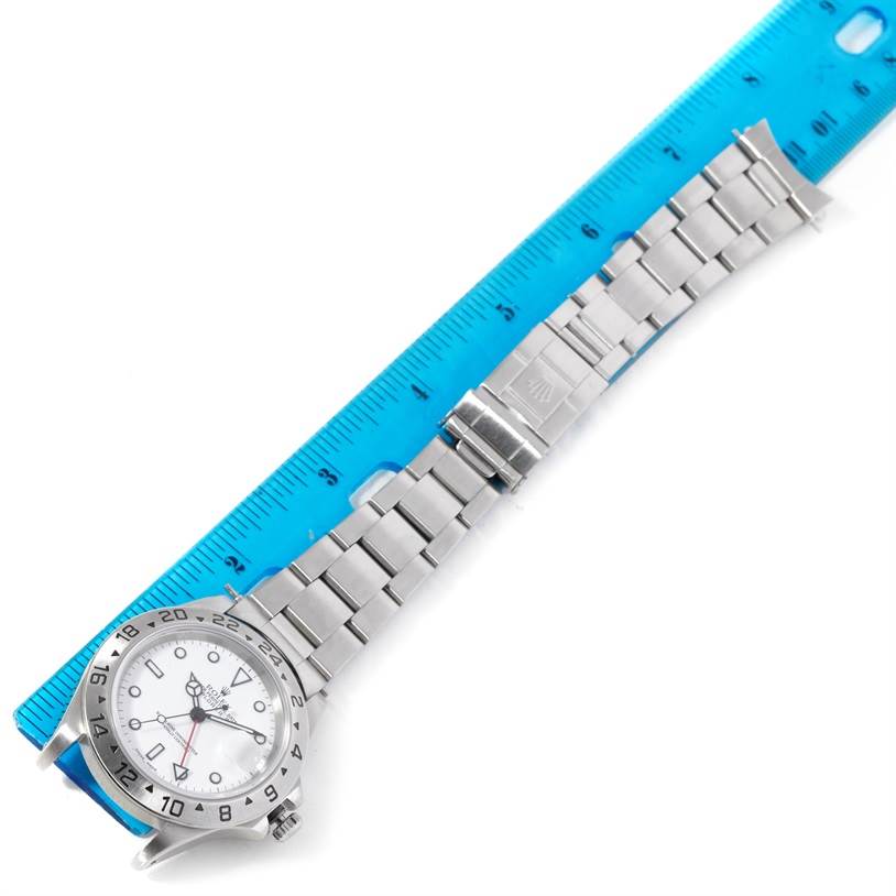 The image shows a Rolex Explorer 16570 Men's Stainless Steel White Dial 16570 Men's Stainless Steel White Dial watch laid flat next to a blue ruler, displaying its face, bracelet, and clasp.