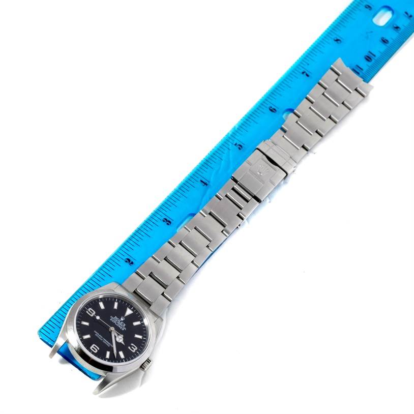 The Rolex Explorer 114270 Men's Stainless Steel Black Dial 114270 Men's Stainless Steel Black Dial watch is shown from a top-down angle with the face, bracelet, and clasp visible next to a ruler for scale.