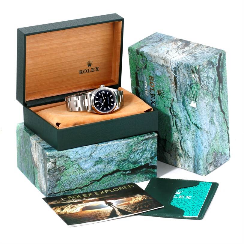 The Rolex Explorer 14270 Men's Stainless Steel Black Dial 14270 Men's Stainless Steel Black Dial watch is shown from a front angle, nestled in its open box with additional packaging and booklets visible.