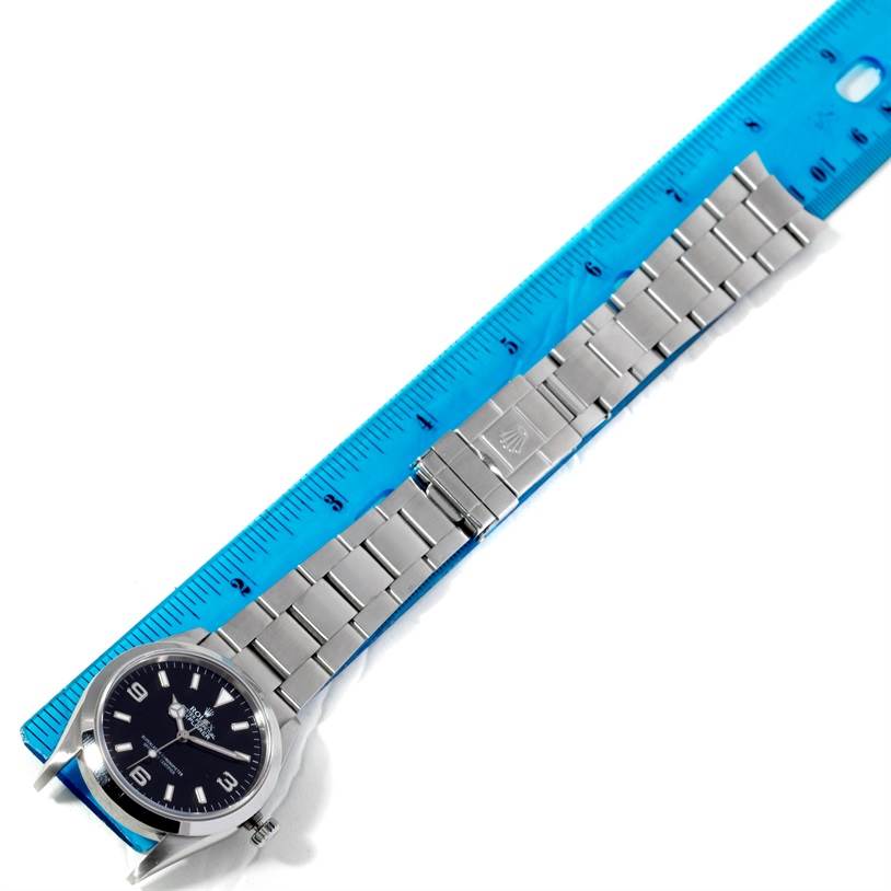 The image shows a side view of a Rolex Explorer 114270 Men's Stainless Steel Black Dial 114270 Men's Stainless Steel Black Dial watch with its metal bracelet laid next to a blue ruler for measurement.