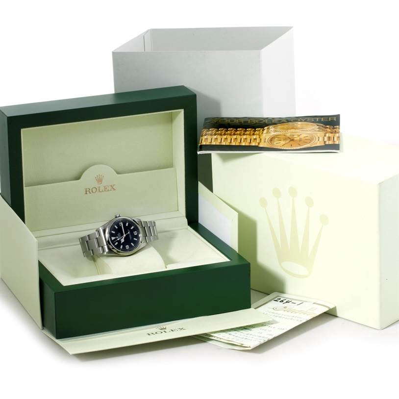 The image shows the Rolex Explorer 114270 Men's Stainless Steel Black Dial 114270 Men's Stainless Steel Black Dial watch along with its box, papers, and a booklet, taken from a front angle.