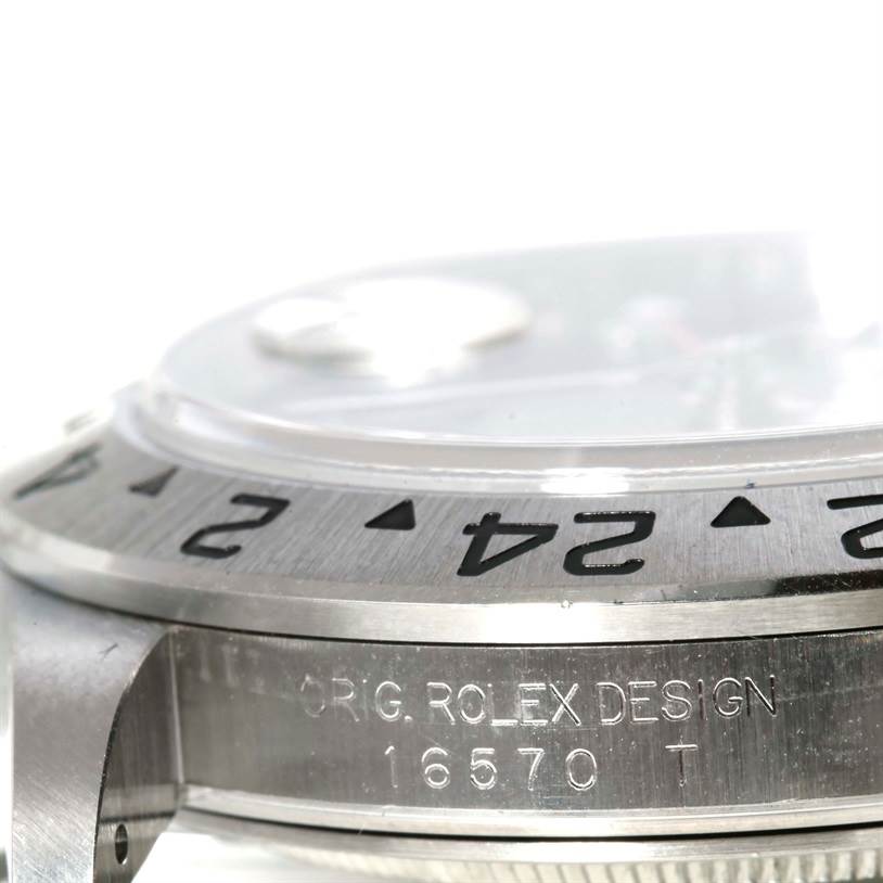 The image shows a close-up of a Rolex Explorer 16570 Men's Stainless Steel White Dial 16570 Men's Stainless Steel White Dial's bezel and the side of the case, engraved with "ORIG. ROLEX DESIGN 16570 T".