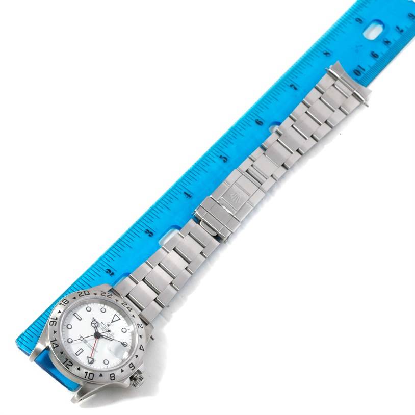 The image shows a Rolex Explorer 16570 Men's Stainless Steel White Dial 16570 Men's Stainless Steel White Dial watch flat on its back with the dial, bezel, bracelet, and clasp visible next to a blue ruler.