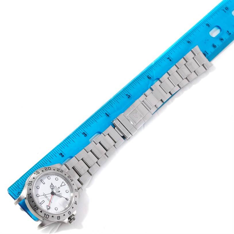 The image shows a Rolex Explorer 16570 Men's Stainless Steel White Dial 16570 Men's Stainless Steel White Dial watch aligned next to a blue ruler, highlighting its bracelet and clasp.
