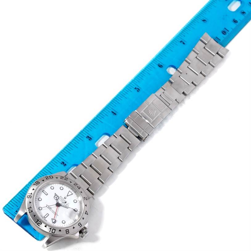 This image shows a Rolex Explorer 16570 Men's Stainless Steel White Dial 16570 Men's Stainless Steel White Dial watch positioned next to a blue ruler, displaying the watch face and entire metal strap.