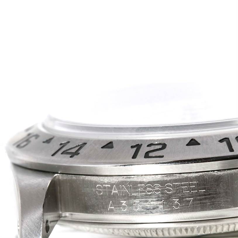 This close-up image of the Rolex Explorer 16570 Men
s Stainless Steel White Dial 16570 Men
s Stainless Steel White Dial watch shows part of the bezel, case, and 
STAINLESS STEEL
 engraving with a serial number.