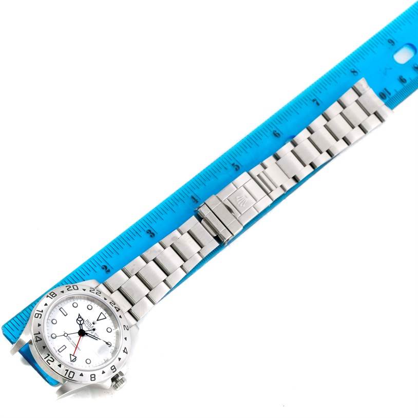 The Rolex Explorer 16570 Men's Stainless Steel White Dial 16570 Men's Stainless Steel White Dial watch is shown from a top-down angle next to a blue ruler, displaying its face, case, and metal bracelet.