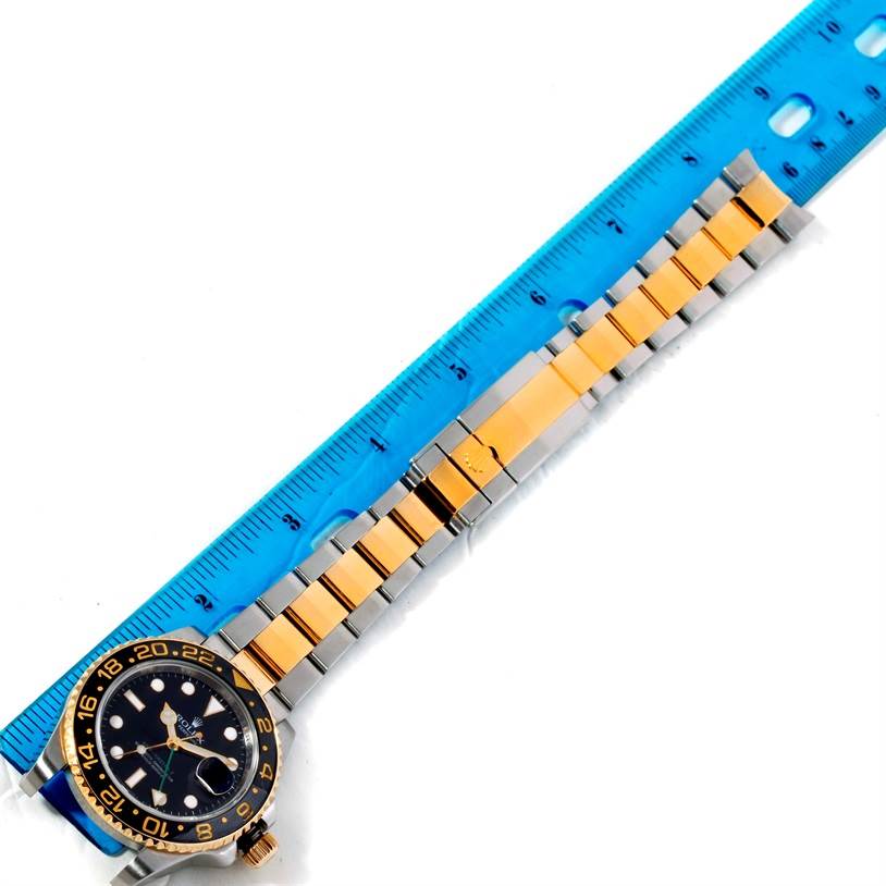The image shows a flat-lay view of a Rolex GMT-Master 116713 Men's Stainless Steel Black Dial 116713 Men's Stainless Steel Black Dial watch with a gold and silver bracelet next to a blue ruler.