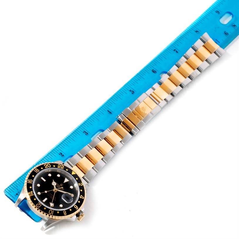 The Rolex GMT-Master 16713 Men's Stainless Steel Black Dial 16713 Men's Stainless Steel Black Dial watch is displayed laid flat with a blue ruler beside it, showcasing the bezel, dial, and bracelet.