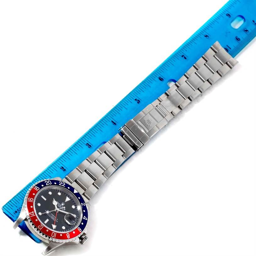 This image shows a top-down view of a Rolex GMT-Master 16710 Men
s Stainless Steel Black Dial 16710 Men
s Stainless Steel Black Dial watch, displaying its face, bezel, and stainless steel bracelet adjacent to a ruler.