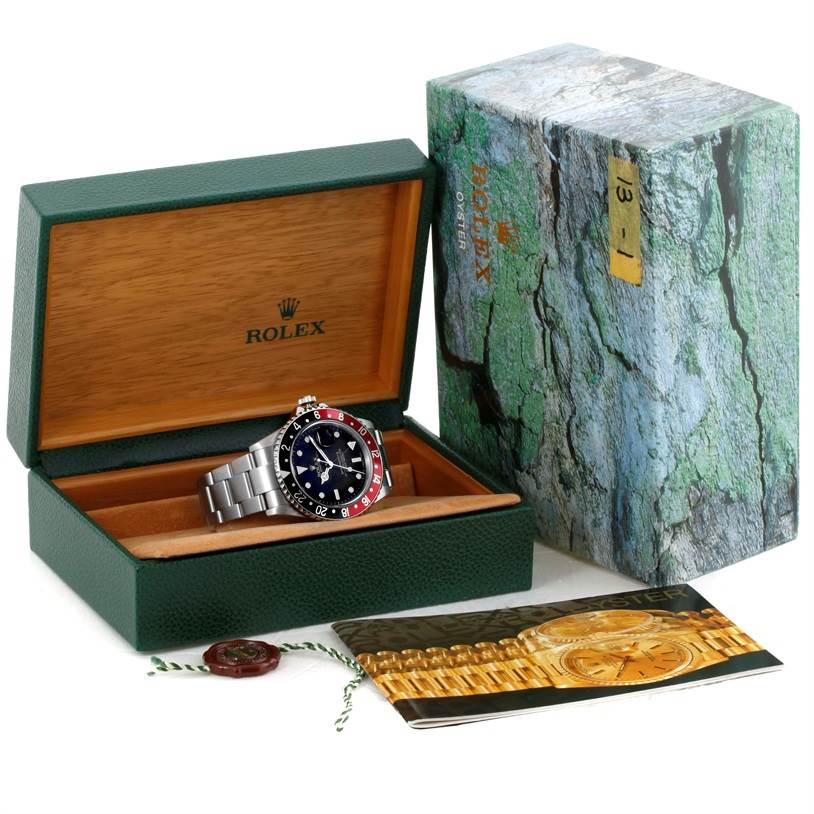 The Rolex GMT-Master 16710 Men's Stainless Steel Black Dial 16710 Men's Stainless Steel Black Dial watch is shown at an angle, inside its open green and wood box, beside its outer box and a booklet.